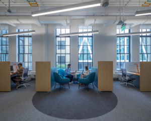 Photo of students sitting at workstation cubicles in an office with large glass windows