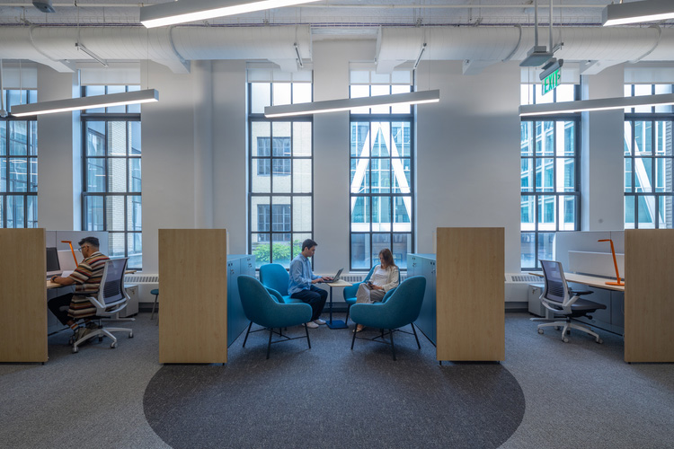 Photo of students sitting at workstation cubicles in an office with large glass windows