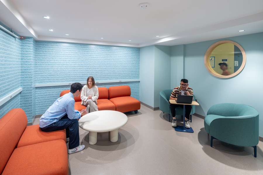 Photo of the small "Pi lounge" with three students sitting in it. Thousands of digits of pi adorn two of the walls.