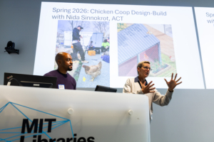 Justin Brazier and Kate Brown stand before a slide at the front of a room, addressing an unseen audience