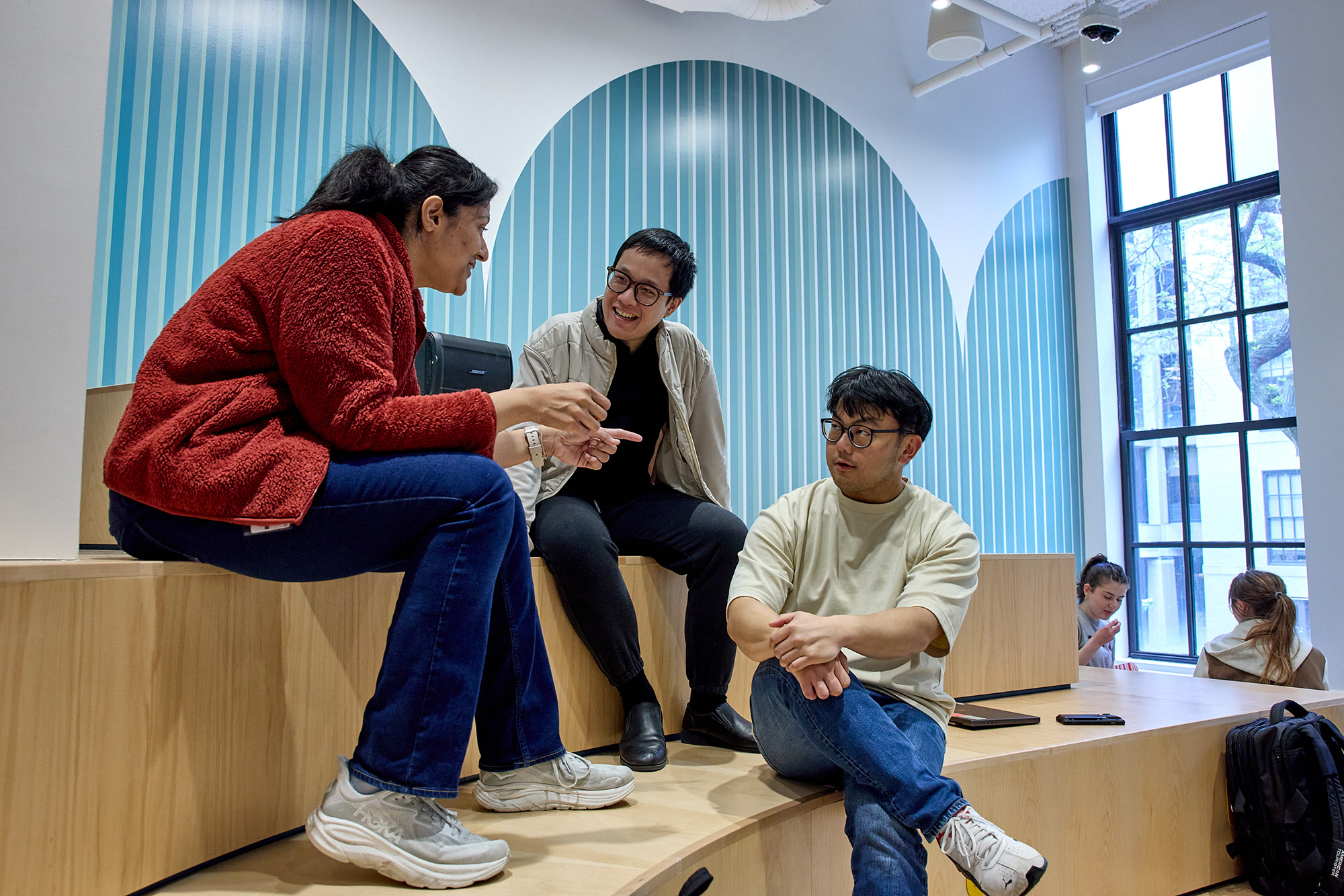 A group of three students sit on the social stairs, chatting.