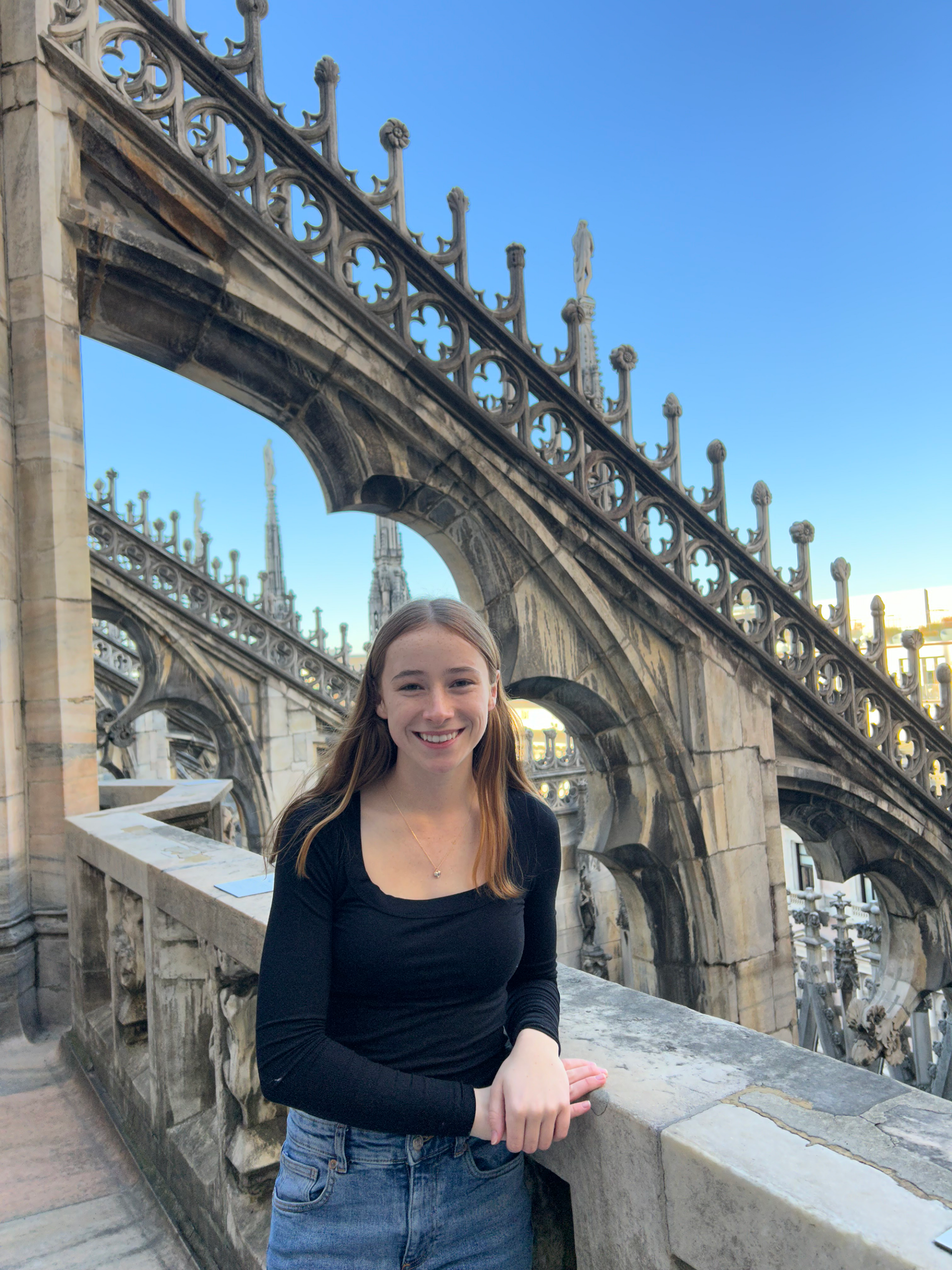 #nivoslider-Xaek6-32748-caption-0 Baily poses outdoors for a photo in Italy, framed by ornate stonework.
