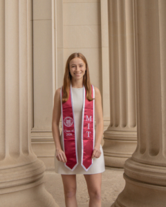 Bailey wears her red MIT graduation sash, standing among the columns of MIT.