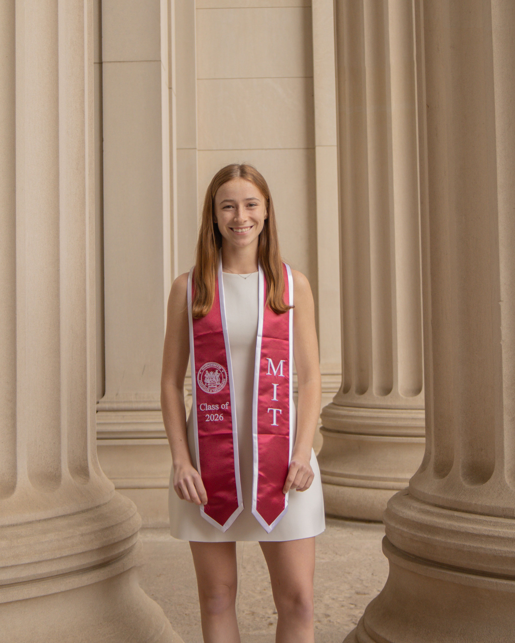 #nivoslider-Xaek6-32748-caption-1 Bailey wears her red MIT graduation sash, standing among the columns of MIT.
